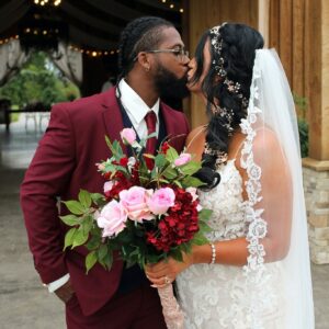 Beautiful couple from Syracuse, NY wearing their wedding attire from Mirror Mirror bridal and kissing. He is in a burgundy suit and she is in a lace wedding dress.