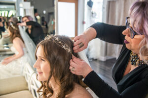 Mirror Mirror bride to be wearing her wedding gown and sitting while her bridal stylist attaches her veil.