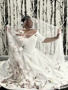 Stunning Mirror Mirror Bride to Be wearing a long embroidered veil and posing dramatically inside the veil.