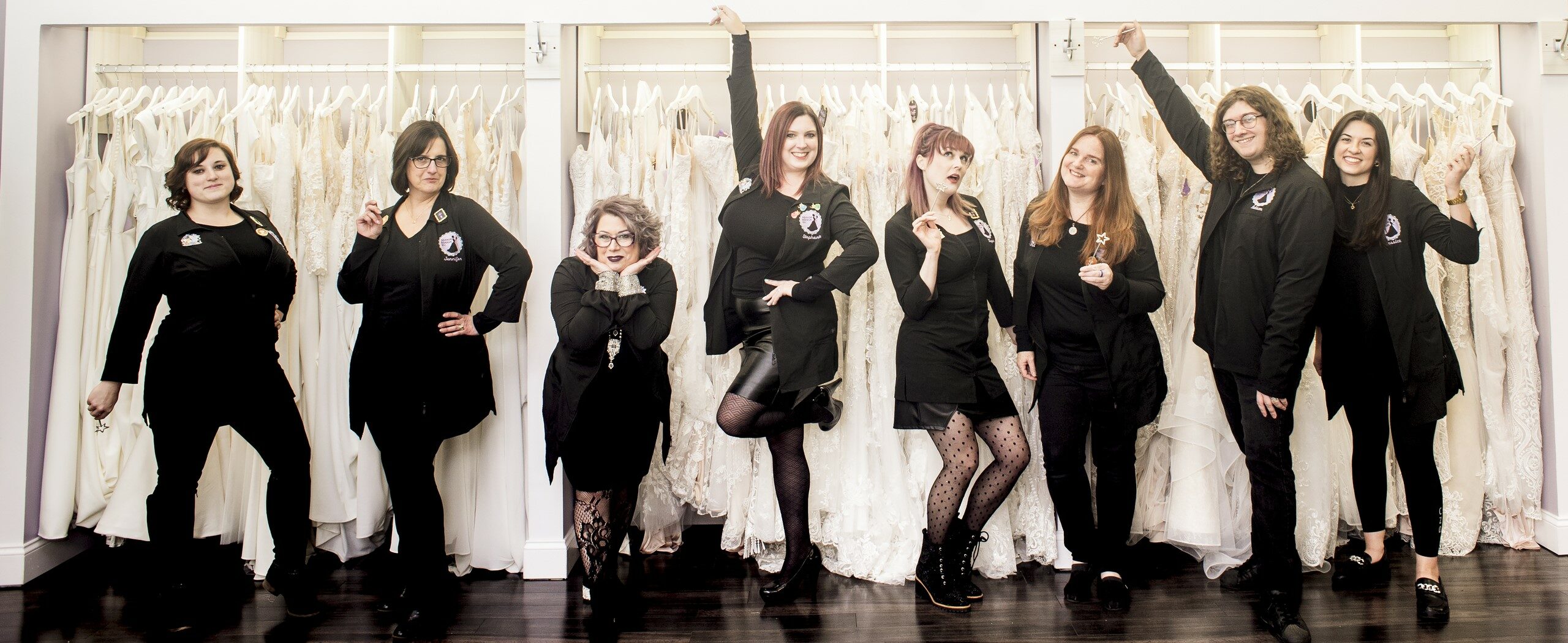 Mirror Mirror Inc. Bridal Boutique team of owners, managers and bridal stylists all posing together in front of their wedding dresses.