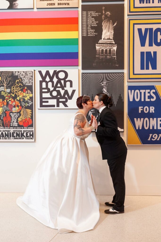 partners in formal attire kissing in front of art wall