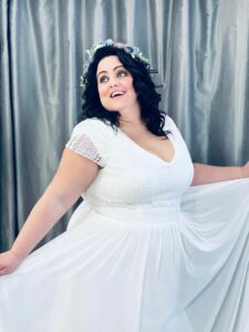 A playful bride to be posing in her maxi dress wedding dress and wearing a spring floral crown.