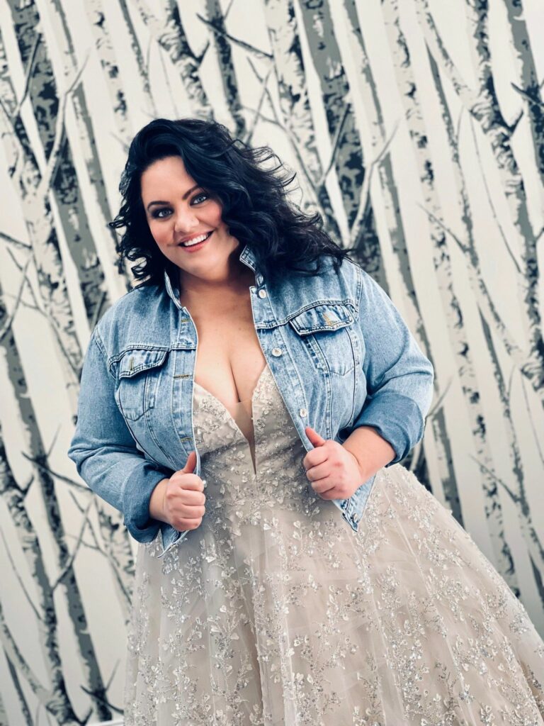 Plus size bride to be wearing her sparkly wedding dress and posing in her jean jacket over.