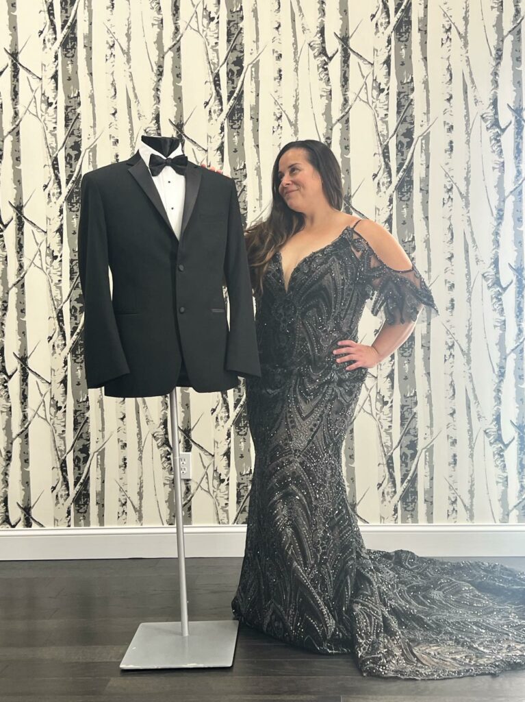 Mirror Mirror bride to be posing in her black wedding dress next to a mannequin wearing a black tuxedo.