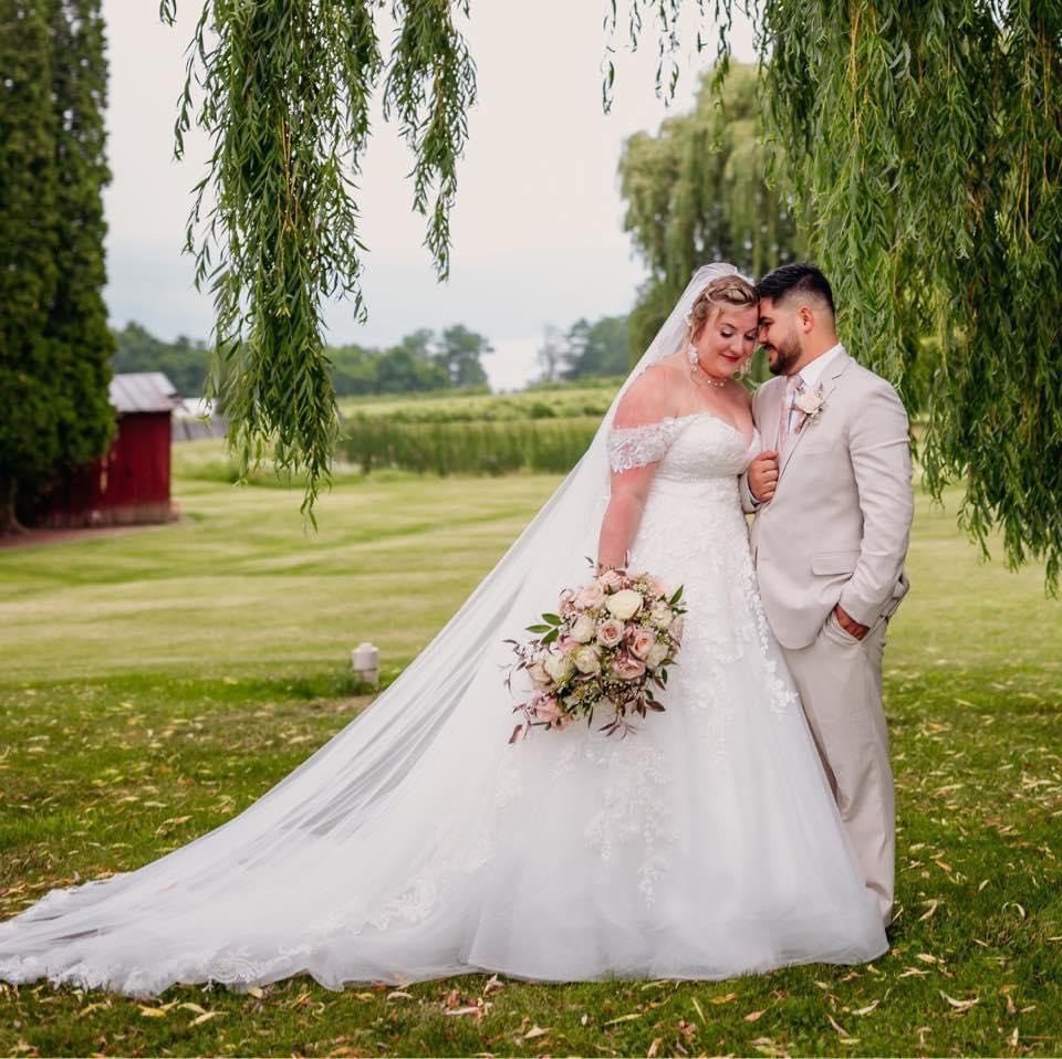 Happy newlywed couple posing in their wedding outfits and leaning their foreheads against each other.