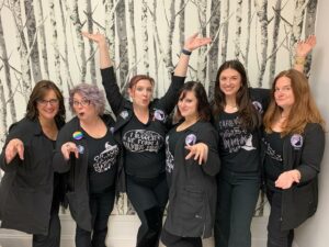 Mirror Mirror Inc. Bridal Boutique's team all posing together against their Into the Woods inspired birch tree wallpaper in Syracuse, NY.